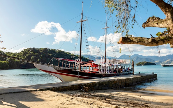 Tourist catamaran docked at pier on Ilha Grande with lush hills in background.