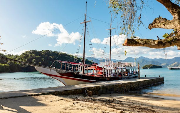 Tourist catamaran docked at pier on Ilha Grande with lush hills in background.