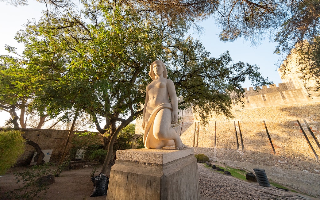 Statue in St George's Castle Gardens with trees and castle wall in Lisbon.