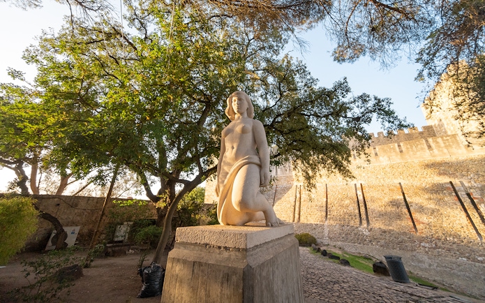 Statue in St George's Castle Gardens with trees and castle wall in Lisbon.