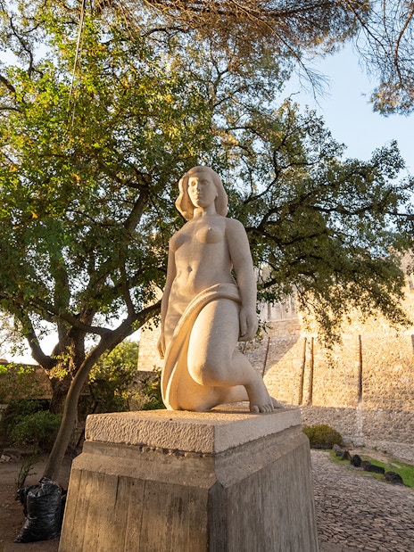 Statue in St George's Castle Gardens with trees and castle wall in Lisbon.
