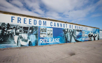Mural with "Freedom Cannot Be Manacled" at Robben Island harbour, depicting historical events.