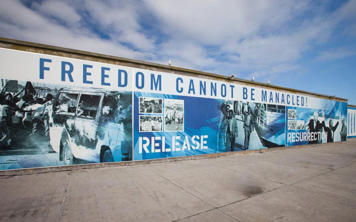 Mural with "Freedom Cannot Be Manacled" at Robben Island harbour, depicting historical events.