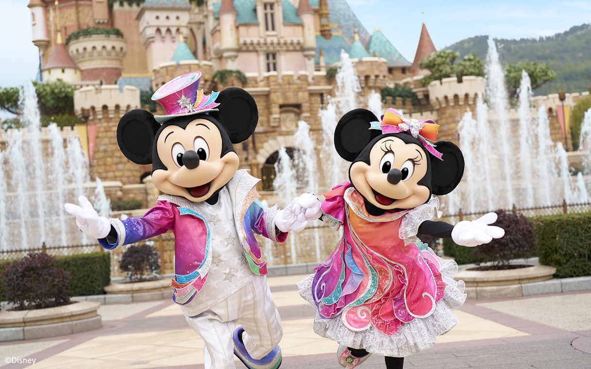 Mickey and Minnie Mouse in colorful outfits at Disneyland Hong Kong with castle backdrop.