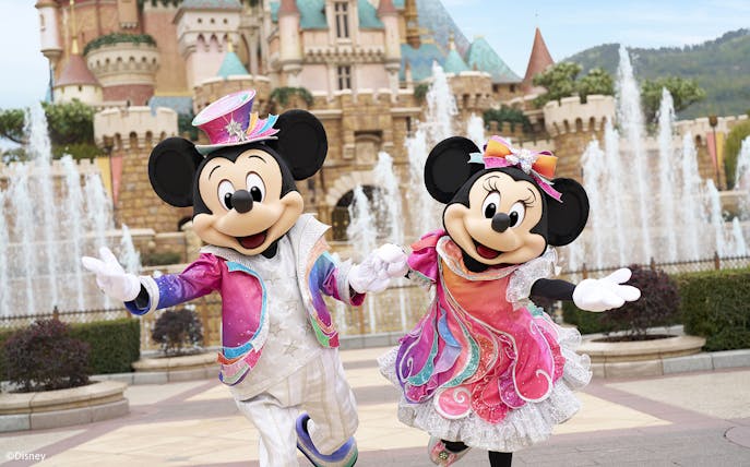 Mickey and Minnie Mouse in colorful outfits at Disneyland Hong Kong with castle backdrop.