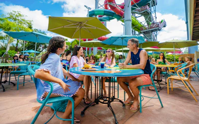 Group dining under umbrellas at Aquatica Orlando with water slides in the background.