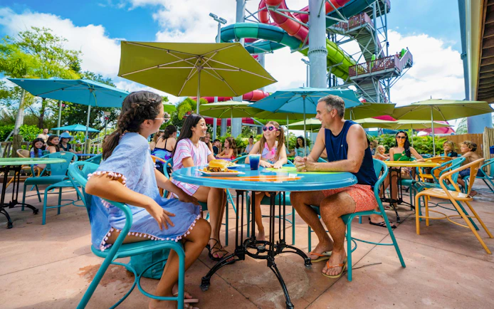 Group dining under umbrellas at Aquatica Orlando with water slides in the background.