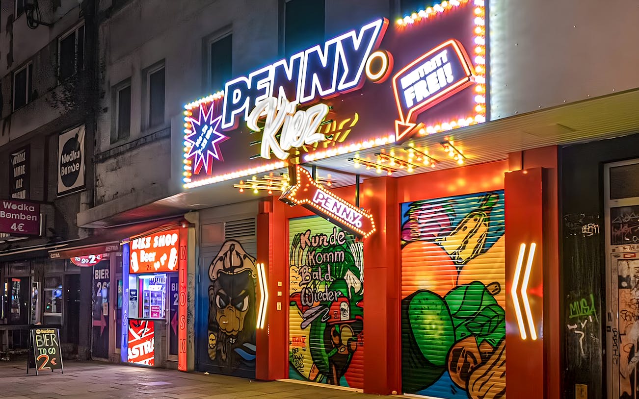 Neon-lit entrance of Penny Kiez shop in Hamburg's nightlife district, featuring vibrant street art.