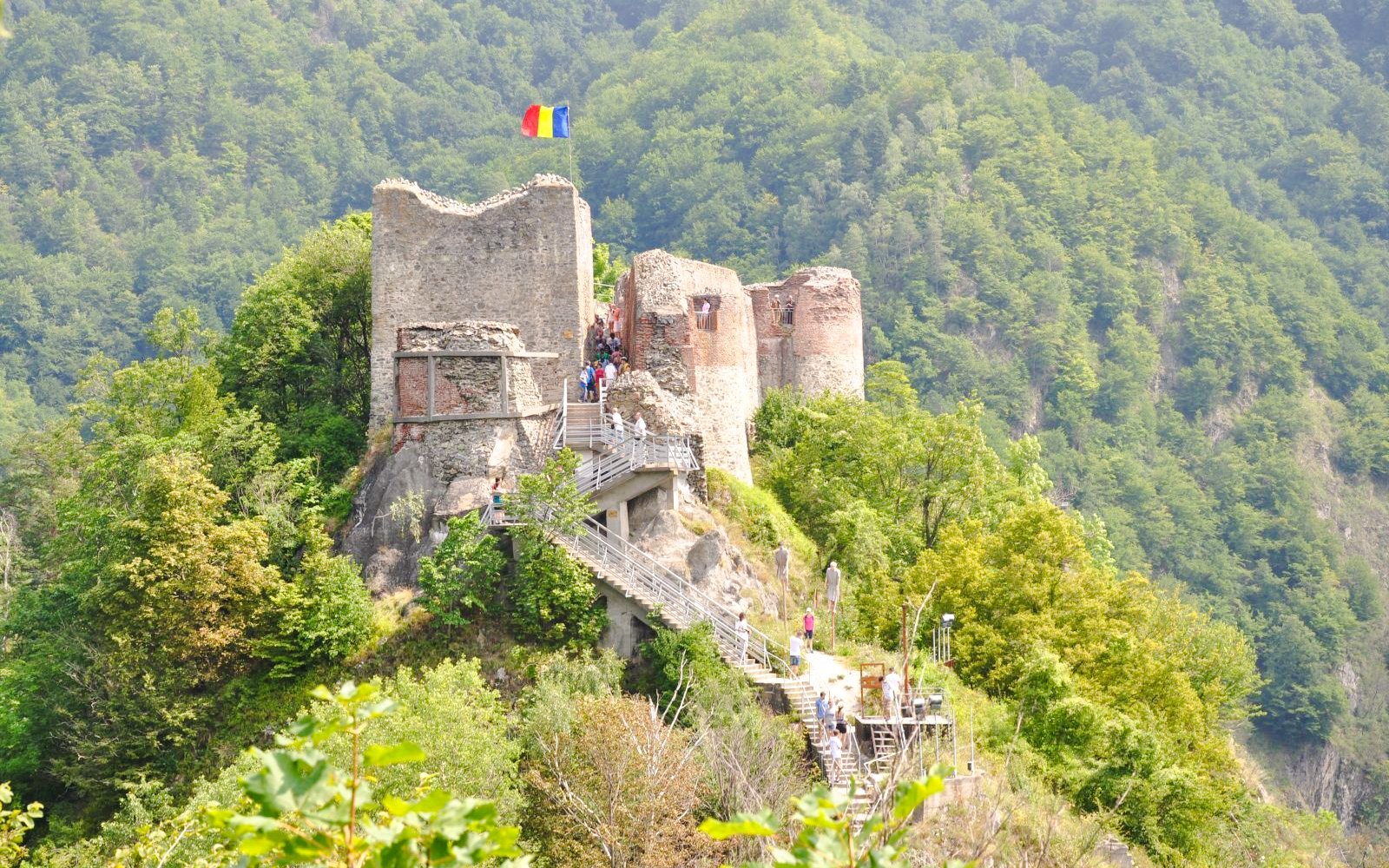Poienari Fortress with Romanian flag, surrounded by lush forest, Romania.
