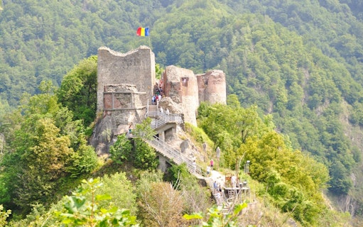 Poienari Fortress with Romanian flag, surrounded by lush forest, Romania.