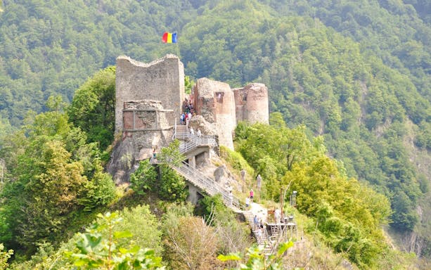 Poienari Fortress with Romanian flag, surrounded by lush forest, Romania.