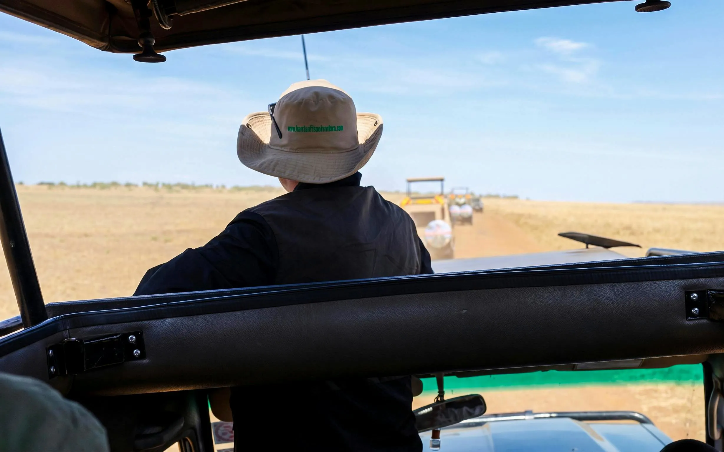 Safari vehicle on a dirt road in Masai Mara, Kenya, with tourists observing wildlife.