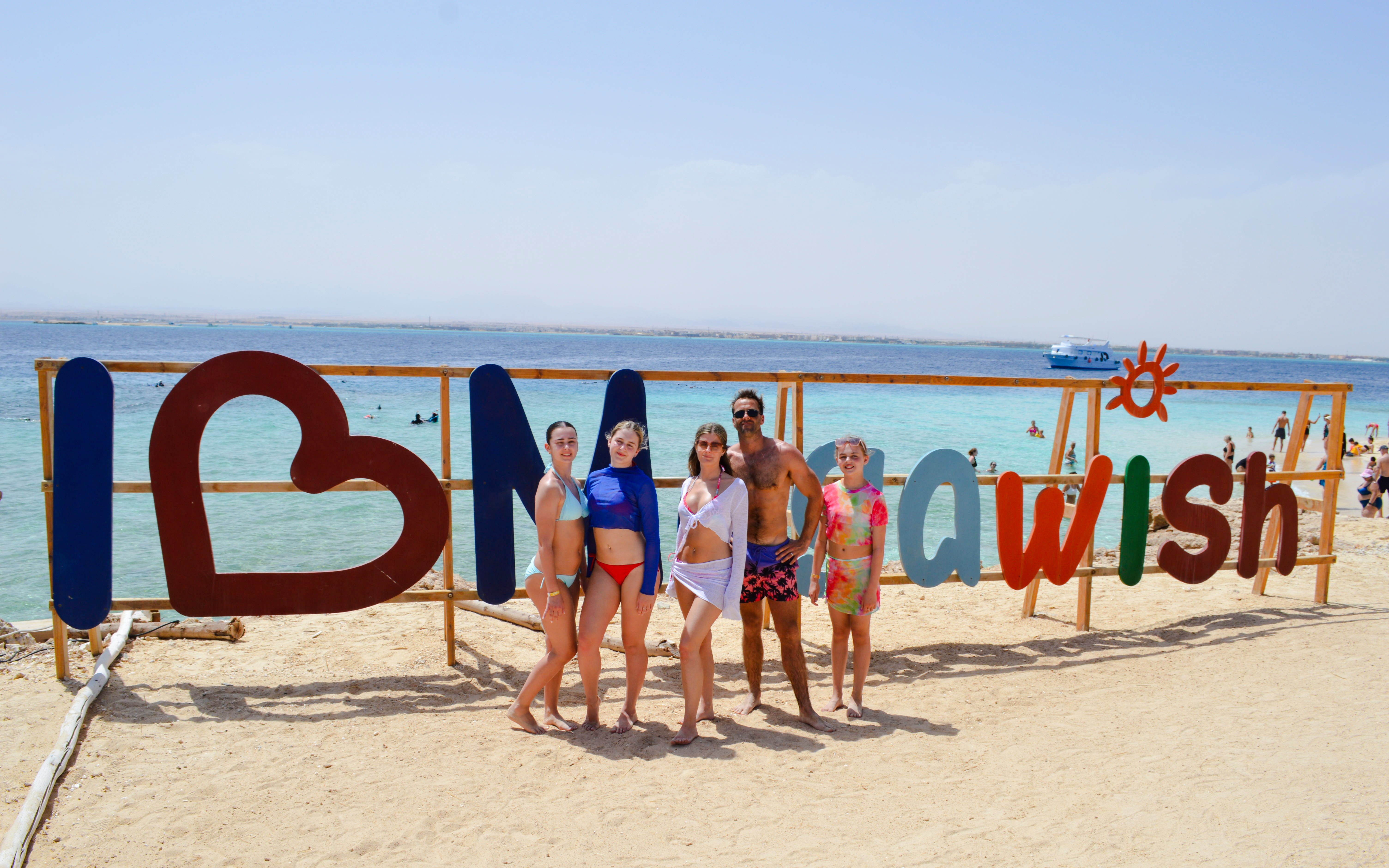 Group enjoying beach at Giftun Islands with "I Love Mahawish" sign in background.