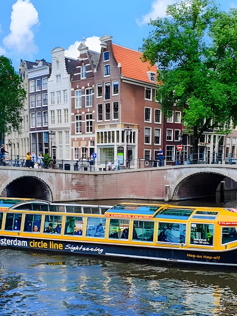 Amsterdam canal cruise boat passing under bridge with historic buildings in background.