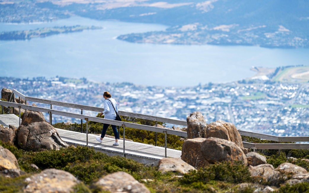 Person walking on a boardwalk with a view of Hobart from Mount Wellington, Tasmania.