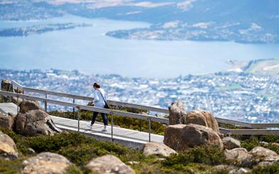Person walking on a boardwalk with a view of Hobart from Mount Wellington, Tasmania.