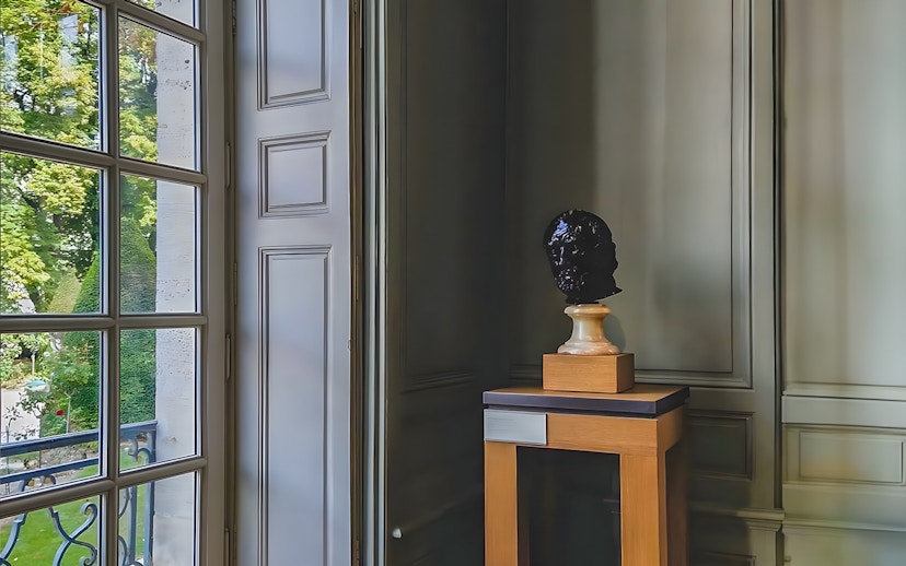 Bust sculpture on display inside Rodin Museum, Paris, near a large window.