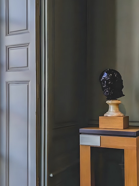 Bust sculpture on display inside Rodin Museum, Paris, near a large window.