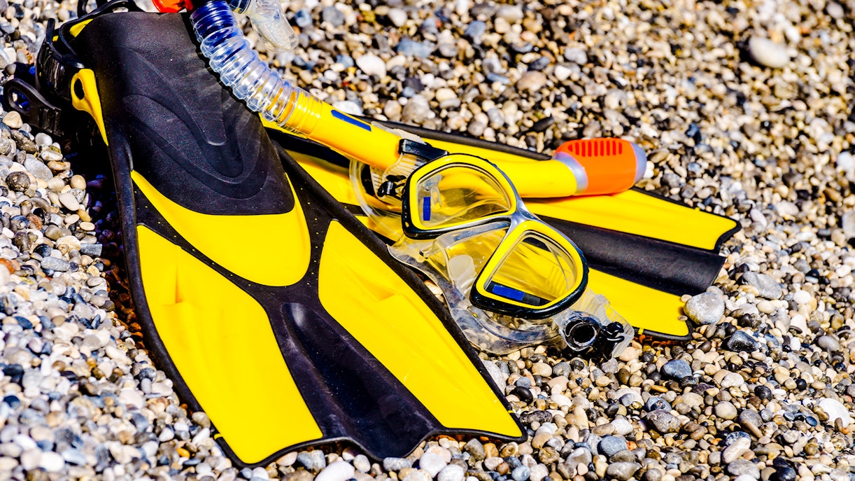 Flippers and snorkeling gear on a pebble beach.