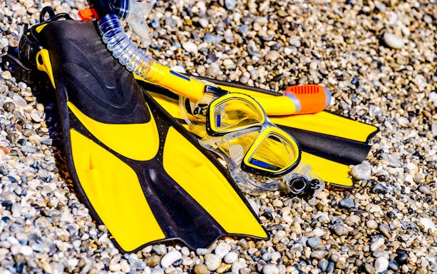 Flippers and snorkeling gear on a pebble beach.
