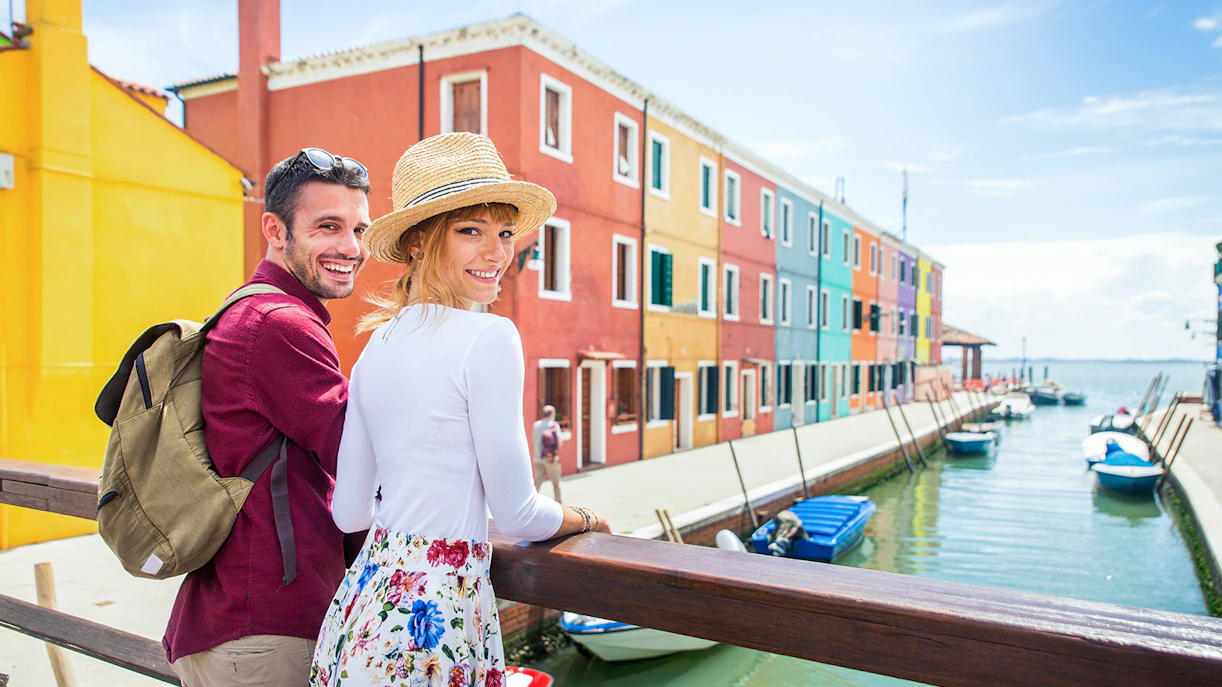 Couple exploring colorful houses along a canal in Burano, Italy.