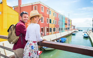 Couple walking along colorful canal in Burano, Italy.