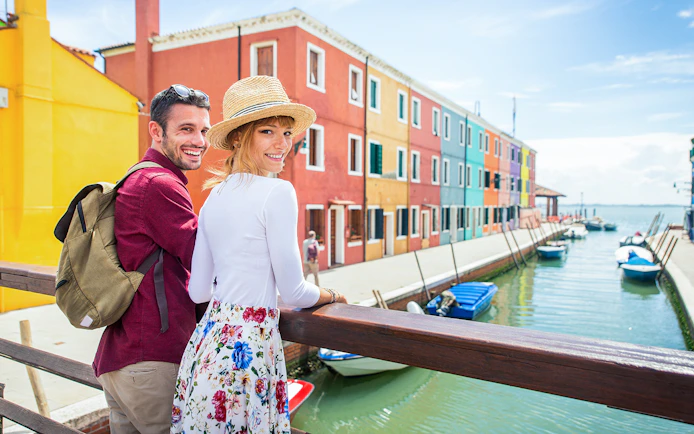 Couple walking along colorful canal in Burano, Italy.