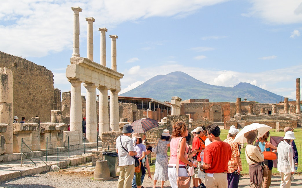 Tour group with guide exploring ancient ruins of Pompeii, Naples, with Mount Vesuvius in background.