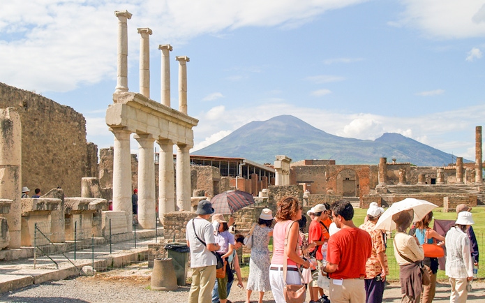 Tour group with guide exploring ancient ruins of Pompeii, Naples, with Mount Vesuvius in background.