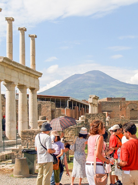 Tour group with guide exploring ancient ruins of Pompeii, Naples, with Mount Vesuvius in background.