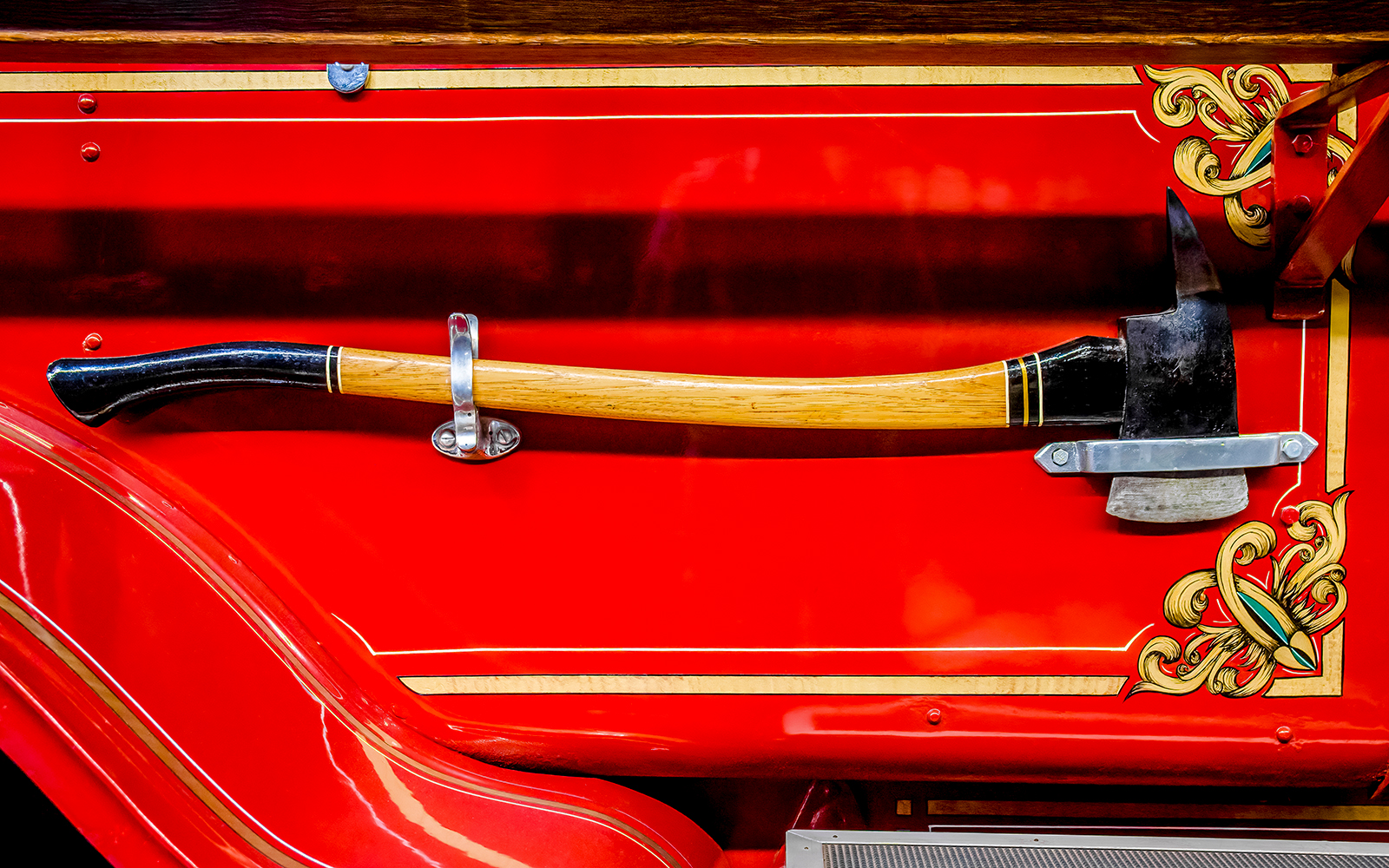 Antique fire engine axe mounted on a decorated red panel.