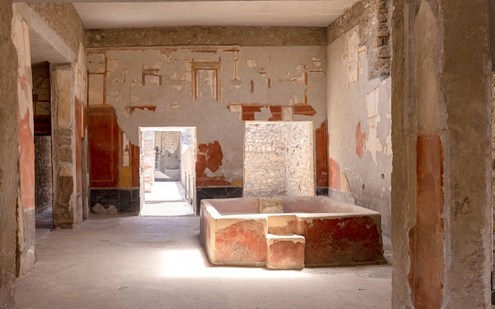 Laundry room with stone bathtub in Stephanus house, Pompeii, featuring ancient frescoes.