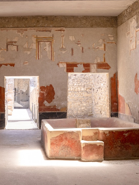 Laundry room with stone bathtub in Stephanus house, Pompeii, featuring ancient frescoes.