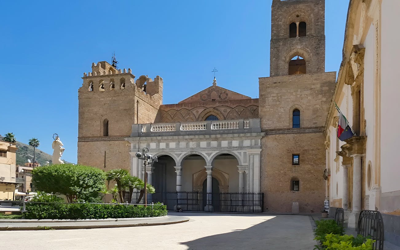 Monreale Cathedral facade with arches and towers on a sunny day.