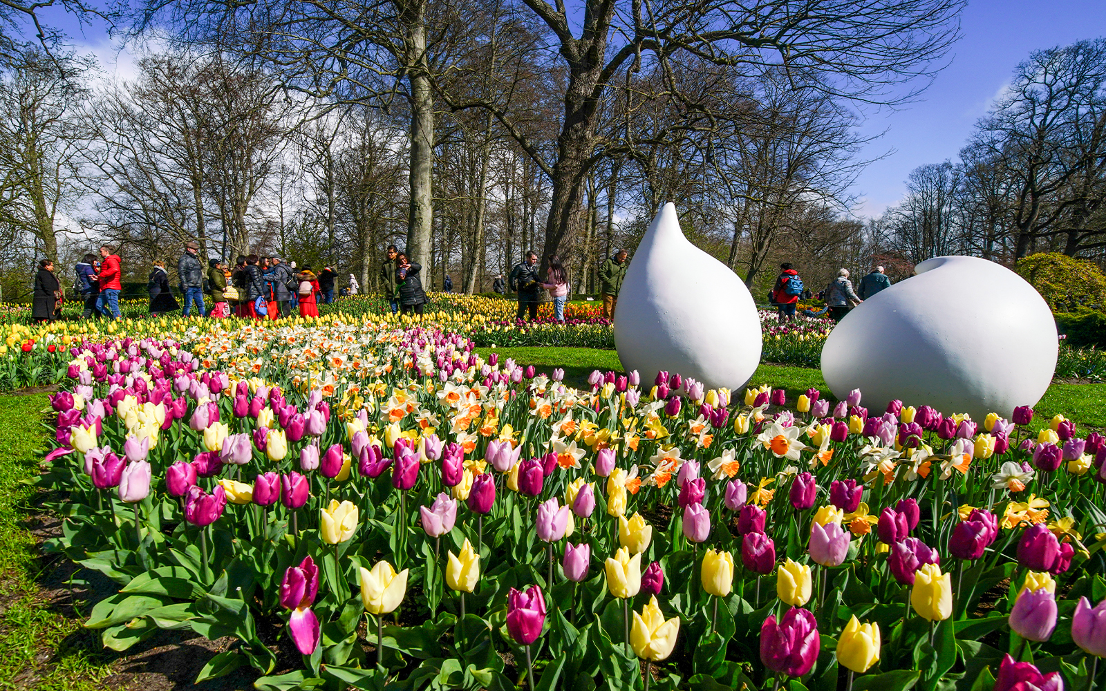 Keukenhof garden with colorful tulips and visitors walking among sculptures.