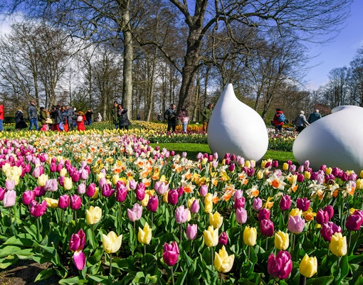 Keukenhof garden with colorful tulips and visitors walking among sculptures.