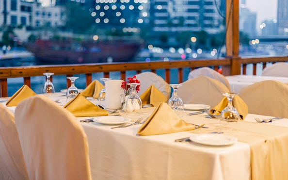 Dinner table setup on Alexandra Dhow Cruise, Dubai Marina, with city lights in the background.