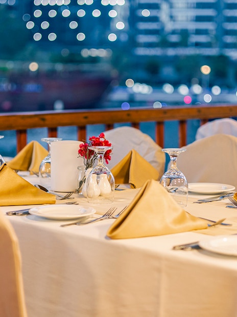 Dinner table setup on Alexandra Dhow Cruise, Dubai Marina, with city lights in the background.