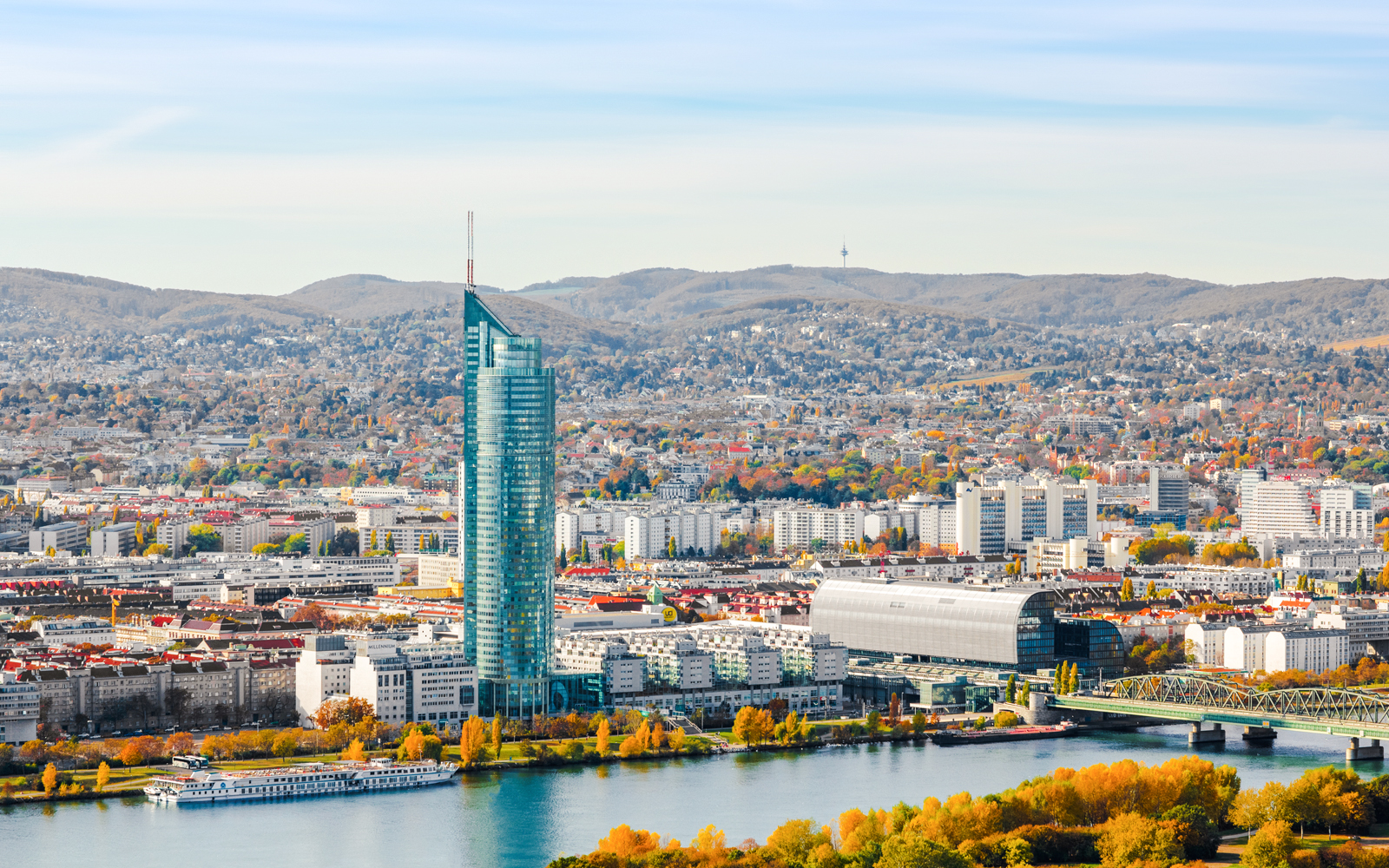 Millennium Tower in Vienna beside the Danube River with cityscape and hills in the background.