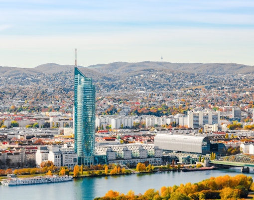 Millennium Tower in Vienna beside the Danube River with cityscape and hills in the background.