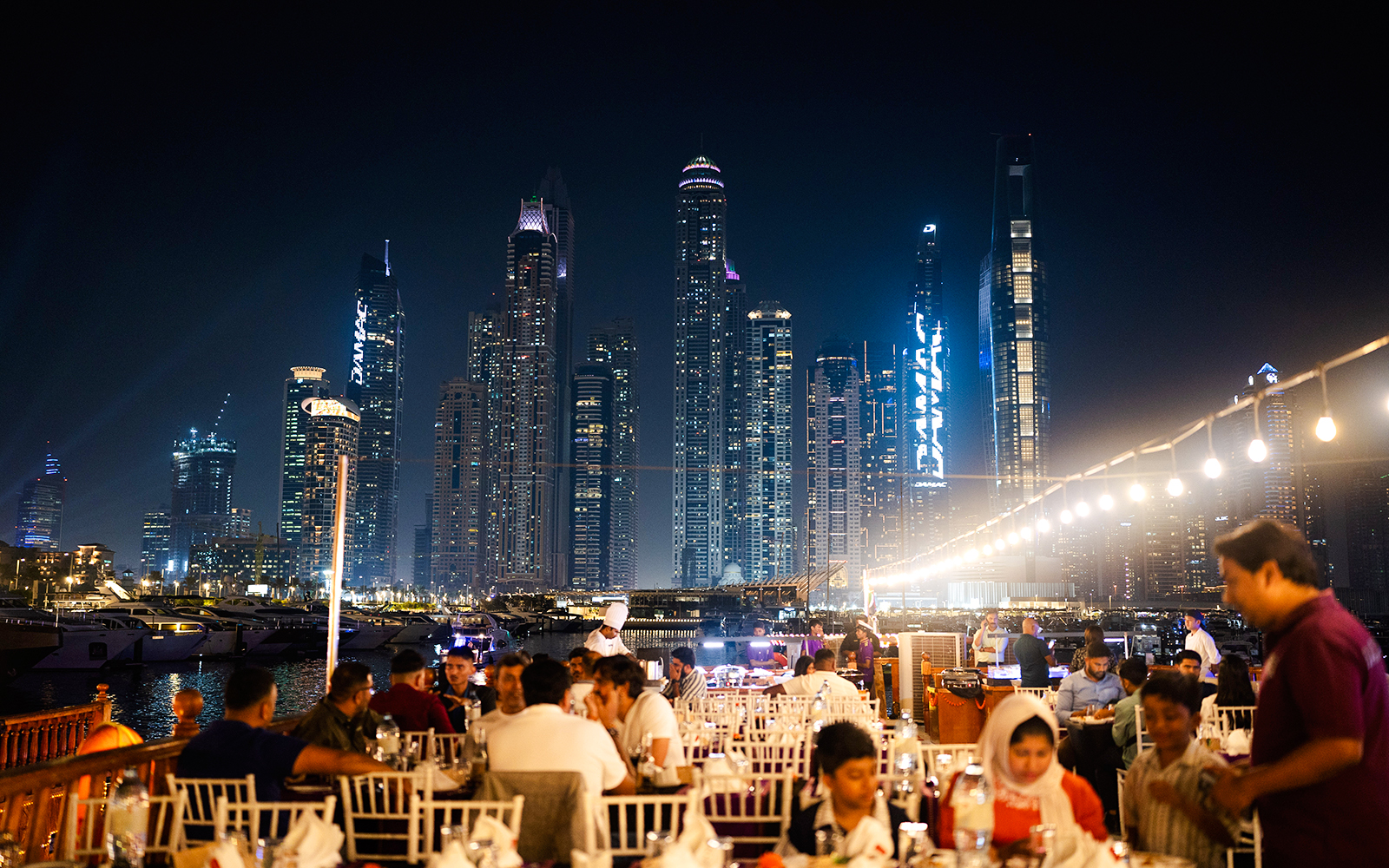 Dubai Marina night cruise with guests dining on a dhow, skyscrapers in the background.