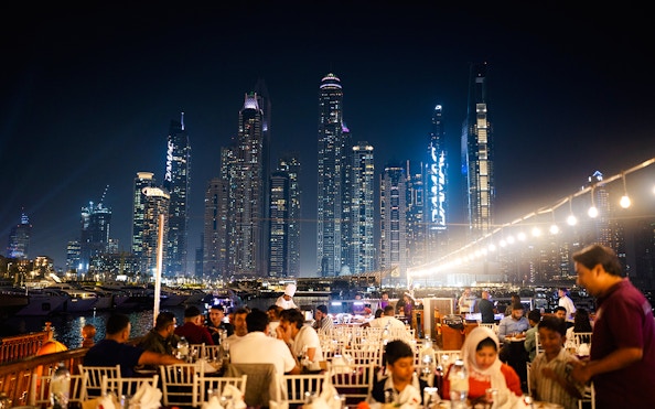 Dubai Marina night cruise with guests dining on a dhow, skyscrapers in the background.