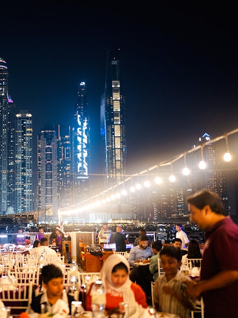 Dubai Marina night cruise with guests dining on a dhow, skyscrapers in the background.