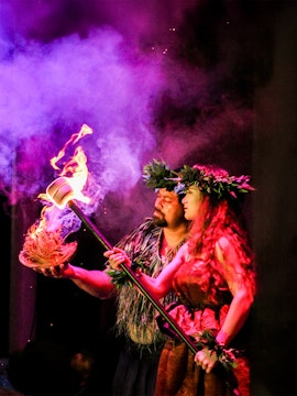 Performers at Moana Luau in Hawaii holding a flaming torch during a traditional Hawaiian ceremony.