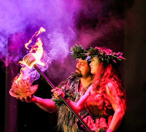 Performers at Moana Luau in Hawaii holding a flaming torch during a traditional Hawaiian ceremony.