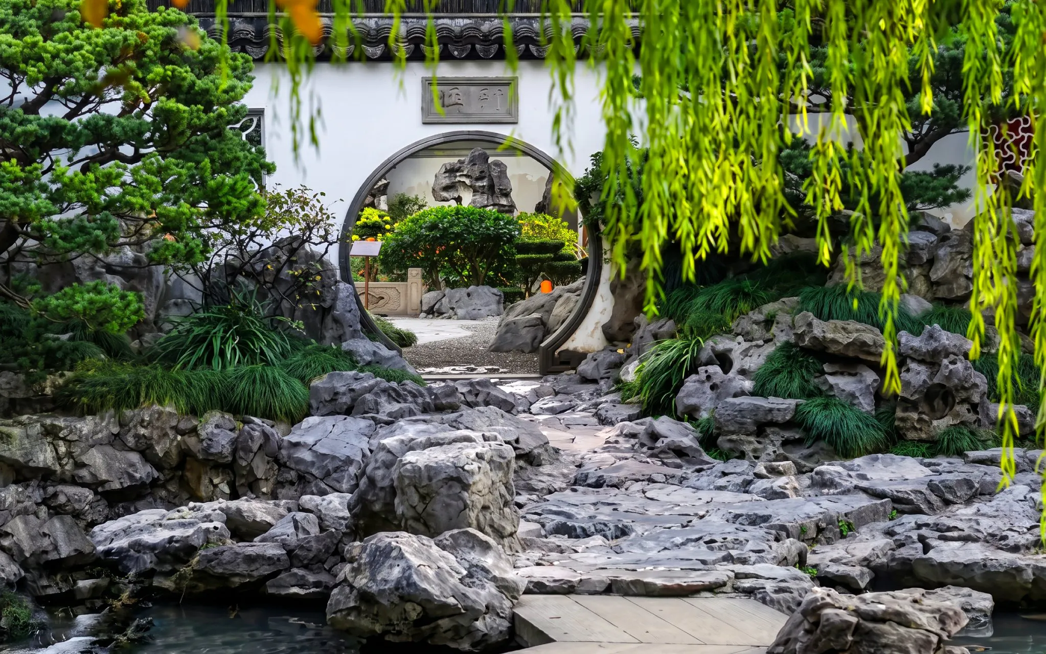 Circular entrance in Yu Garden, Shanghai, China, surrounded by rocks and lush greenery.