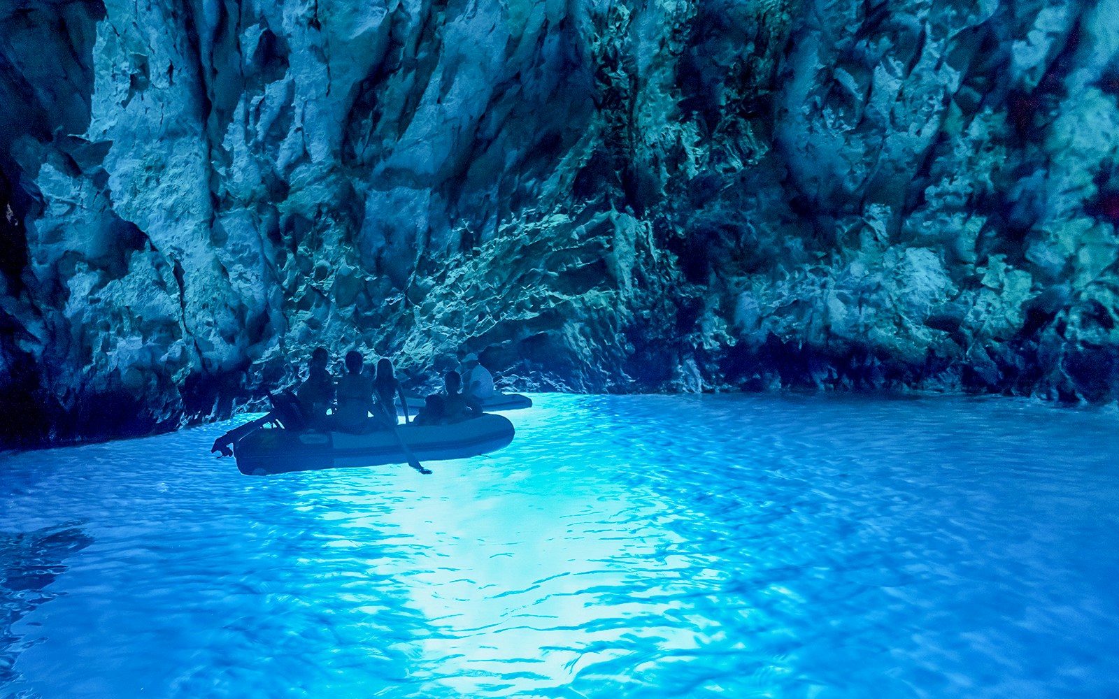 Boat tour inside Blue Cave, Dubrovnik, with illuminated blue water and rocky walls.
