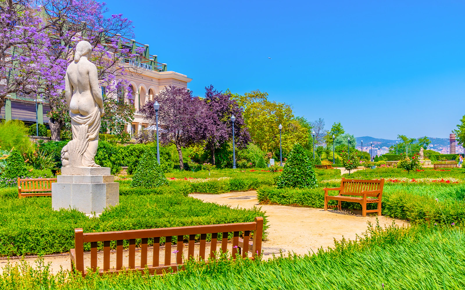 Statue and benches in Jardins del Mirador, Barcelona, with city view.