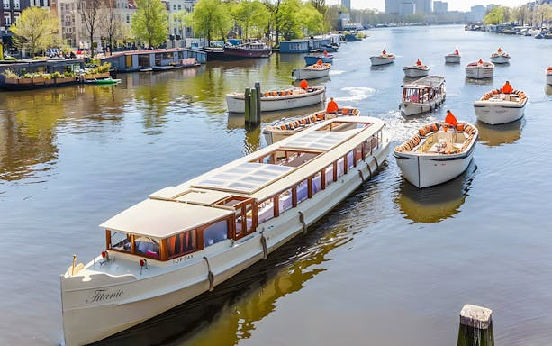 Saloon boat cruising through Amsterdam canals with historic buildings in view.