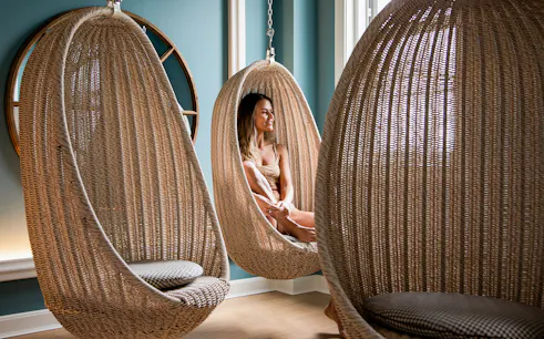 Person relaxing in a wicker hanging chair at QC New York spa.
